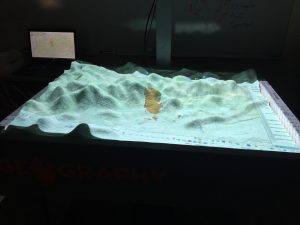 A close up view of an AR sandbox displaying color-coded topography