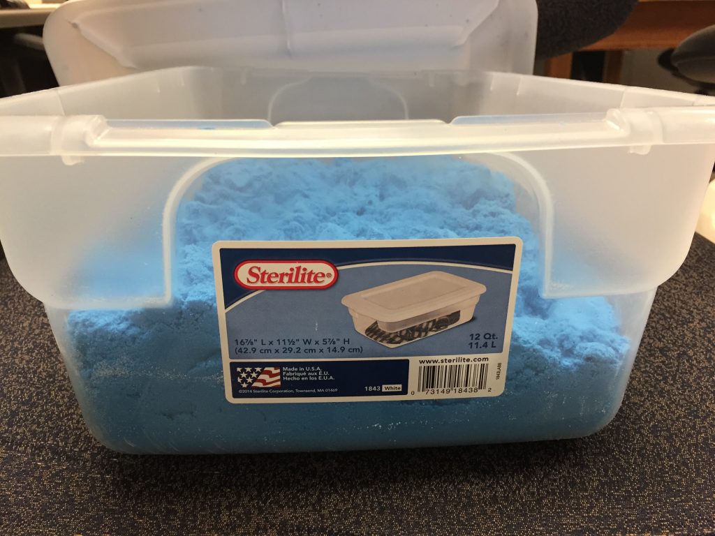 A plastic tub with blue sand inside