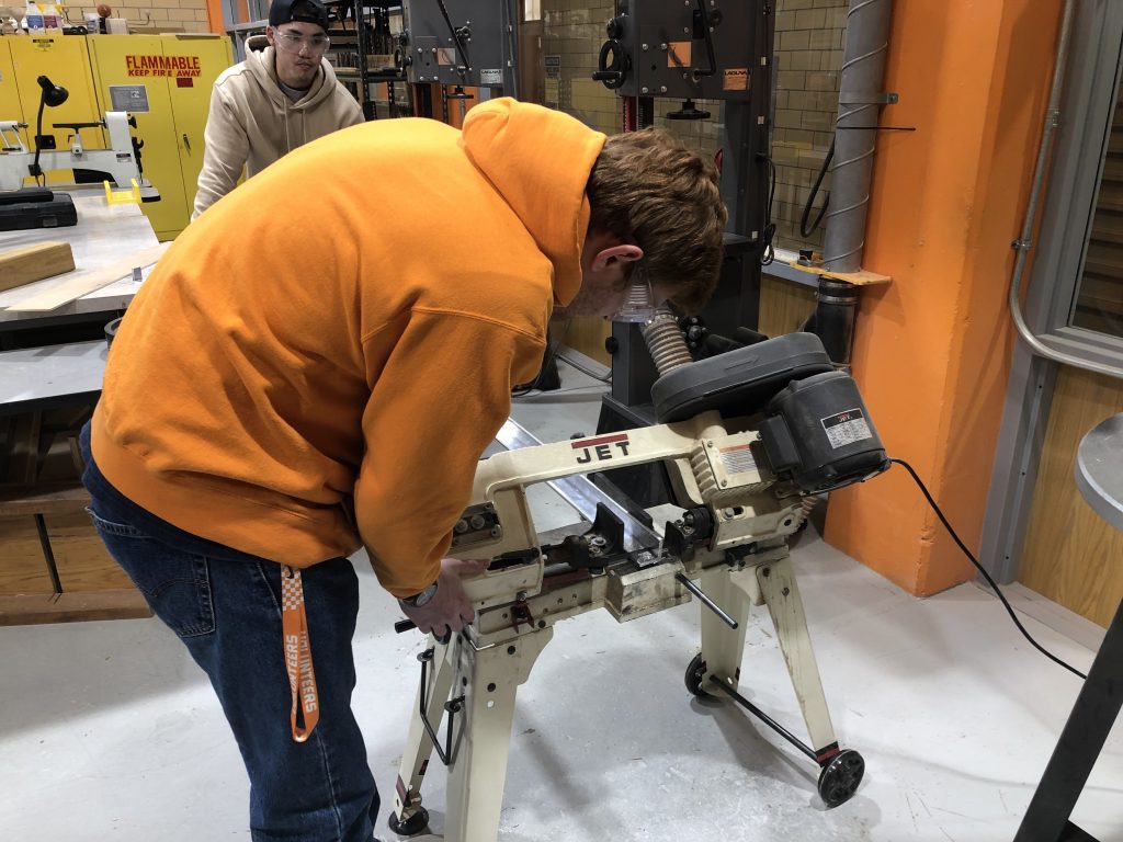 student uses bandsaw to cut aluminum tubing
